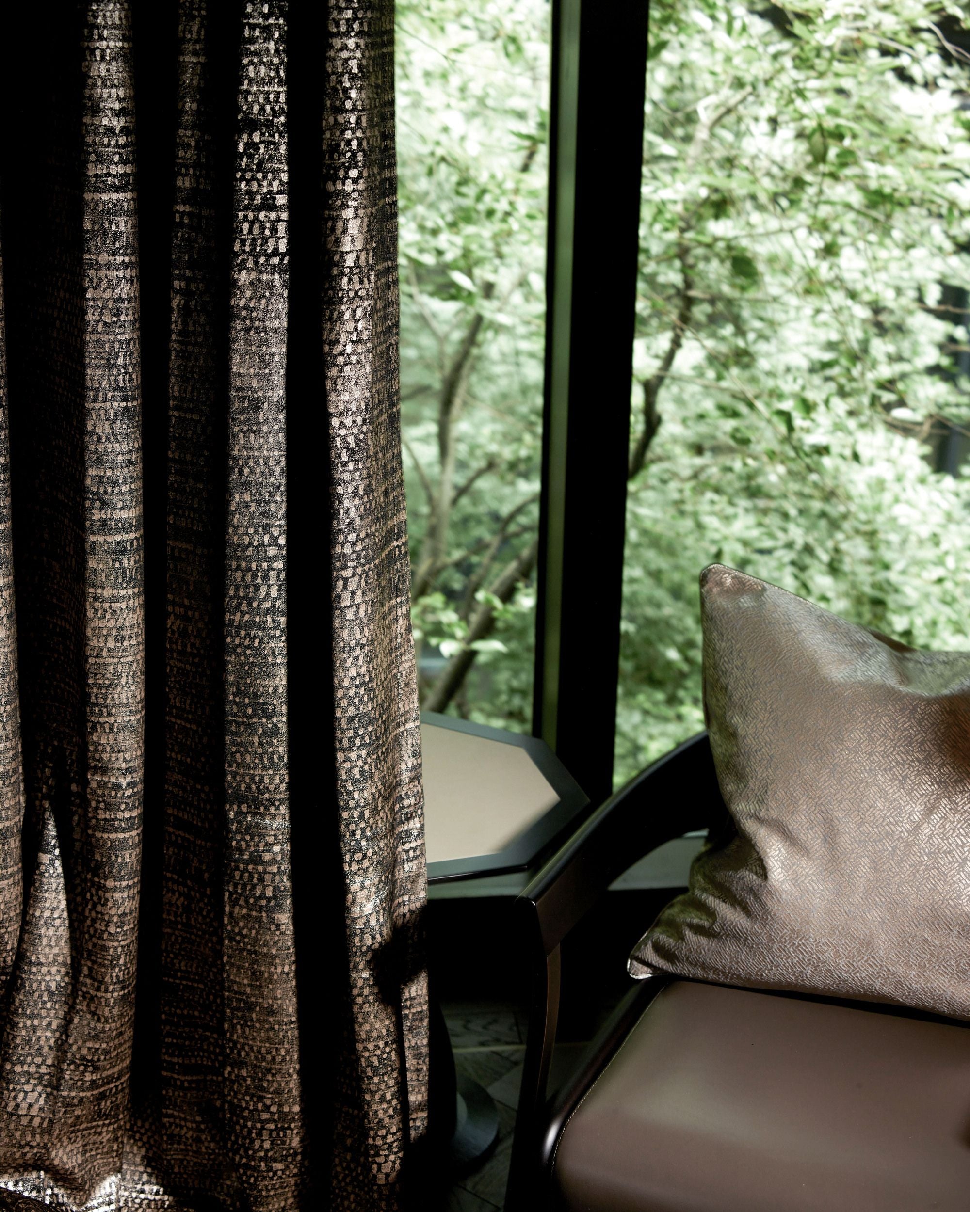 Pebbles foil printed velvet custom curtain, dark with shimmering pattern, beautifully draped, next to a matching decorative pillow.