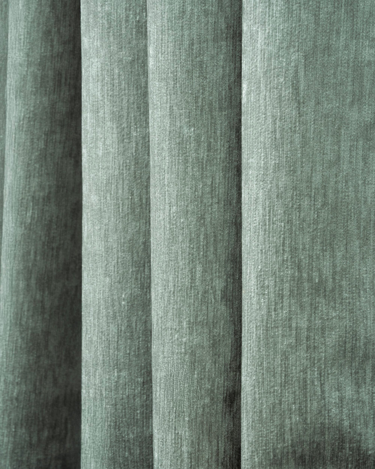 Close-up of richly draped green heavyweight velvet custom blackout curtain fabric, showing soft texture and elegant folds.