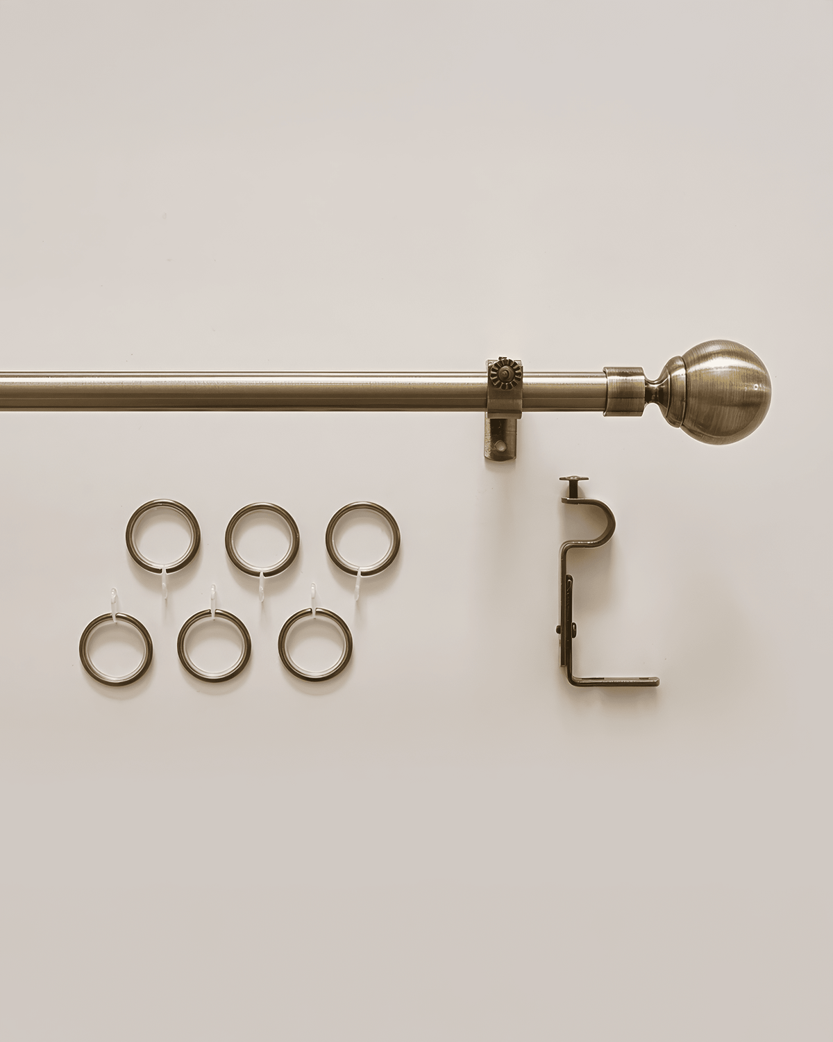 Antique brass custom curtain rod with elegant ball finial, mounting bracket, and six matching drapery rings for window treatments.