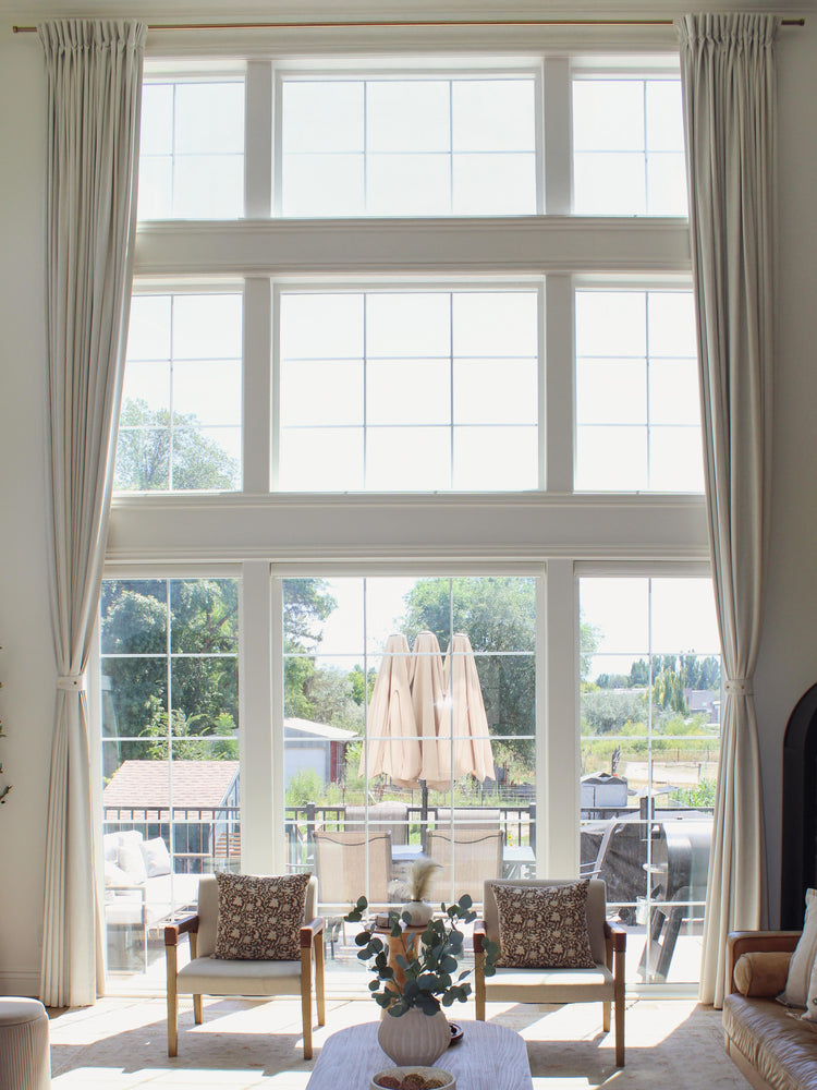 Off-white custom linen blend drapery on tall living room windows, styled with tie-backs for elegant light control.