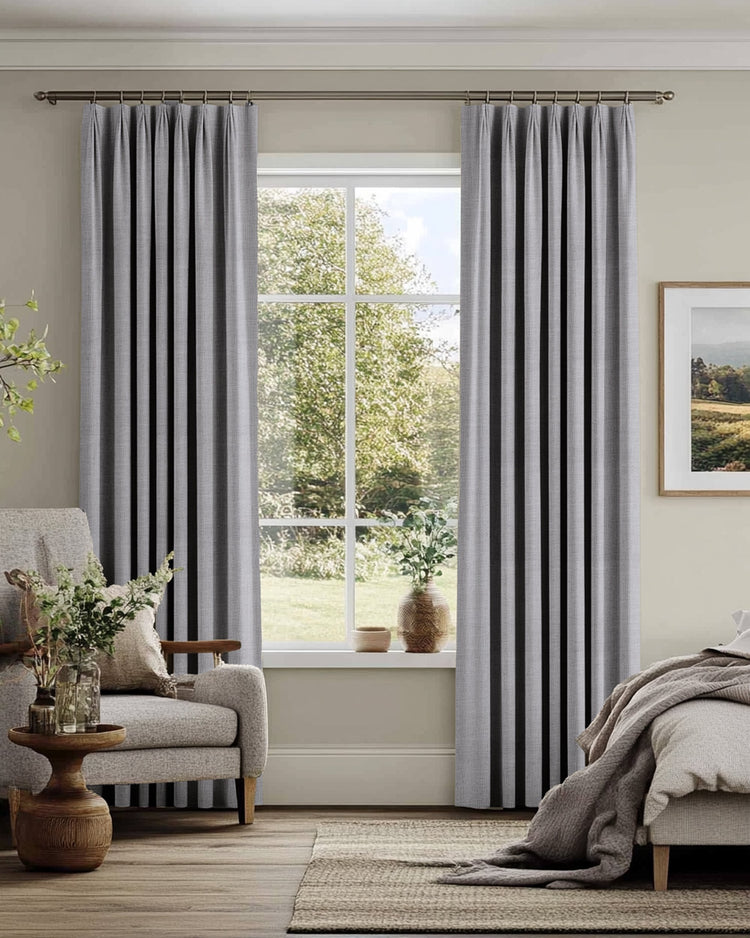 Elegant light grey custom linen blend drapery with a French pleat header hanging on a rod in a neutral room.