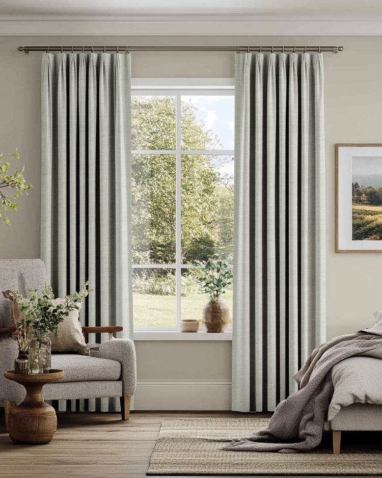 Custom linen blend pinch pleat drapery framing a sunlit window, enhancing a serene living space with elegant window treatments.