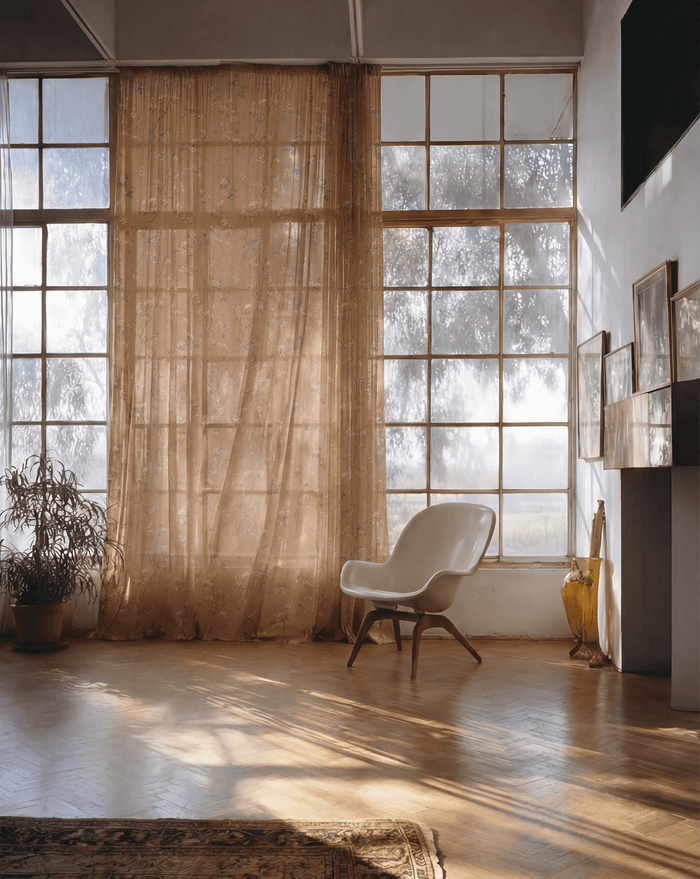 Amber floral patterned sheer custom curtain by TheHues filtering sunlight on large windows in a bright minimalist room.