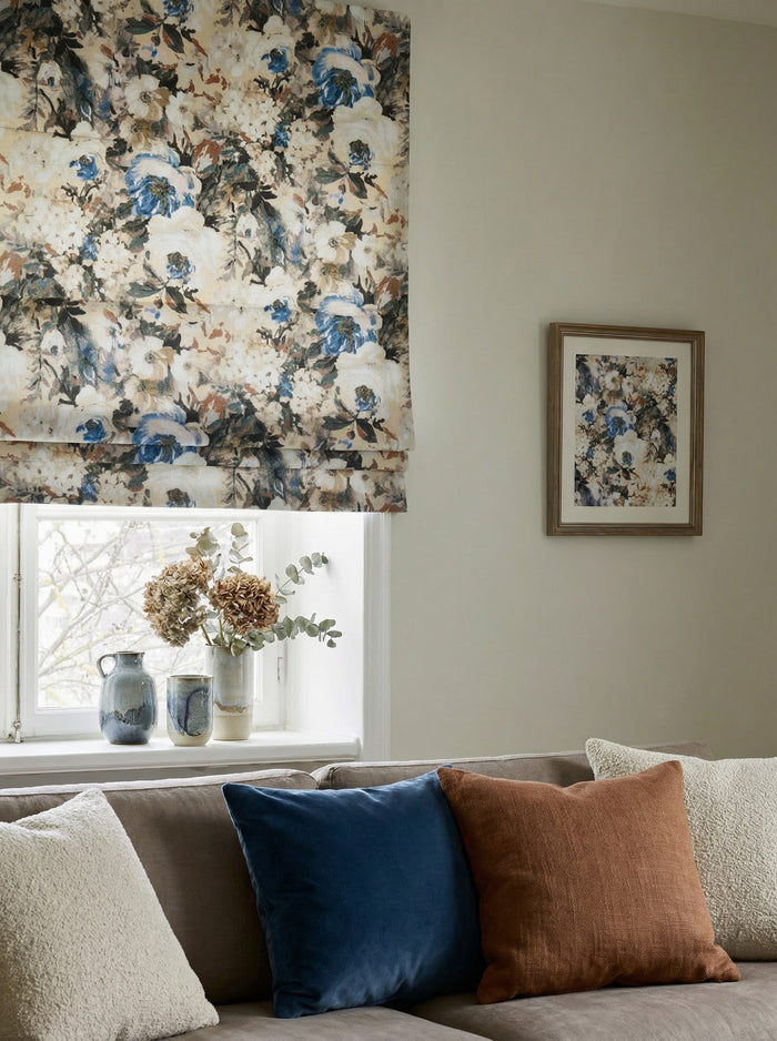 Custom floral flat fold roman shade in canvas velvet with a blue watercolor print above a window and living room sofa.