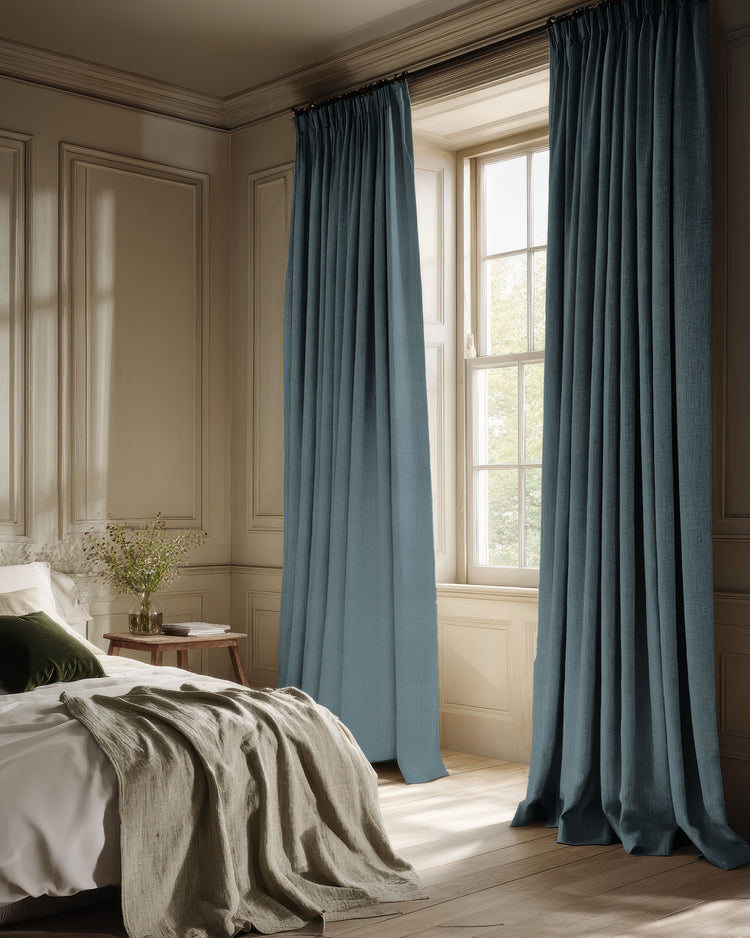 Elegant blue Voy blackout linen look custom curtains with structured pleats frame a bedroom window, enhancing light control & privacy.