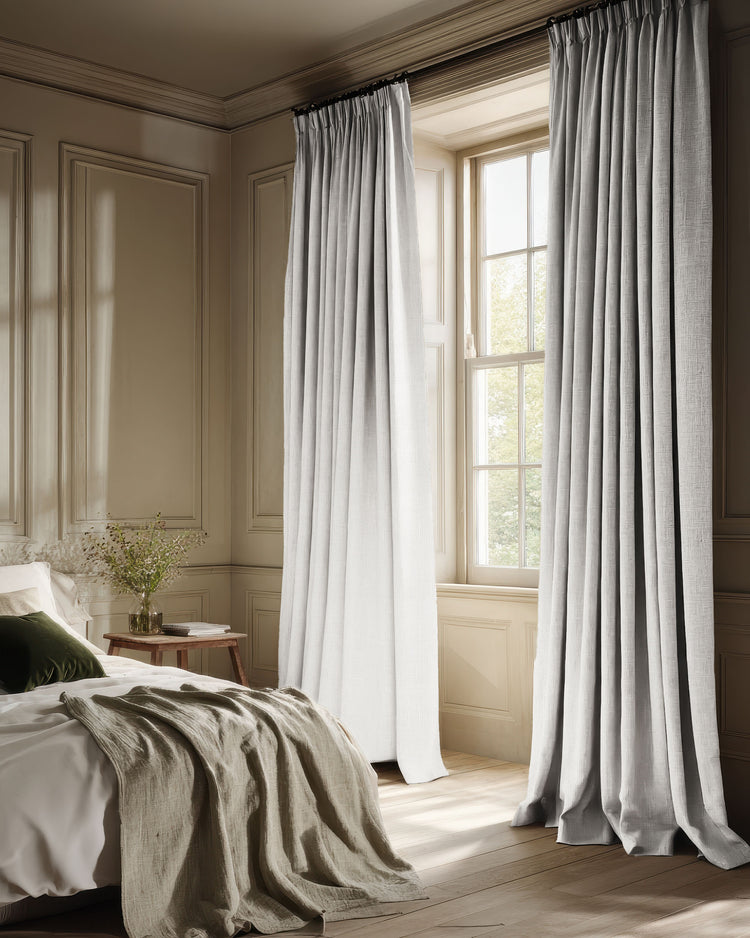 Floor-length light gray custom blackout curtains with a textured linen look in a cozy bedroom with paneled walls.