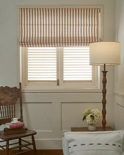Custom-made Milano flat fold Roman shade in striped linen blend fabric, showcasing crisp folds over white window shutters.