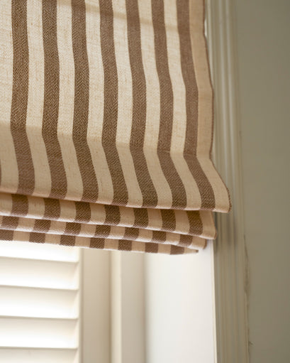 Close-up of custom flat fold Roman shade, showcasing linen blend fabric with elegant vertical beige & brown stripes and subtle texture.