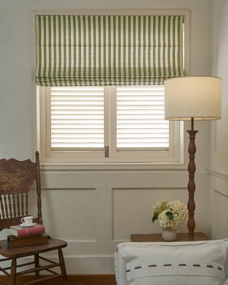 Milano Flat Fold Linen Blend Custom Roman Shade with green and natural stripes, elegantly installed above white window shutters.