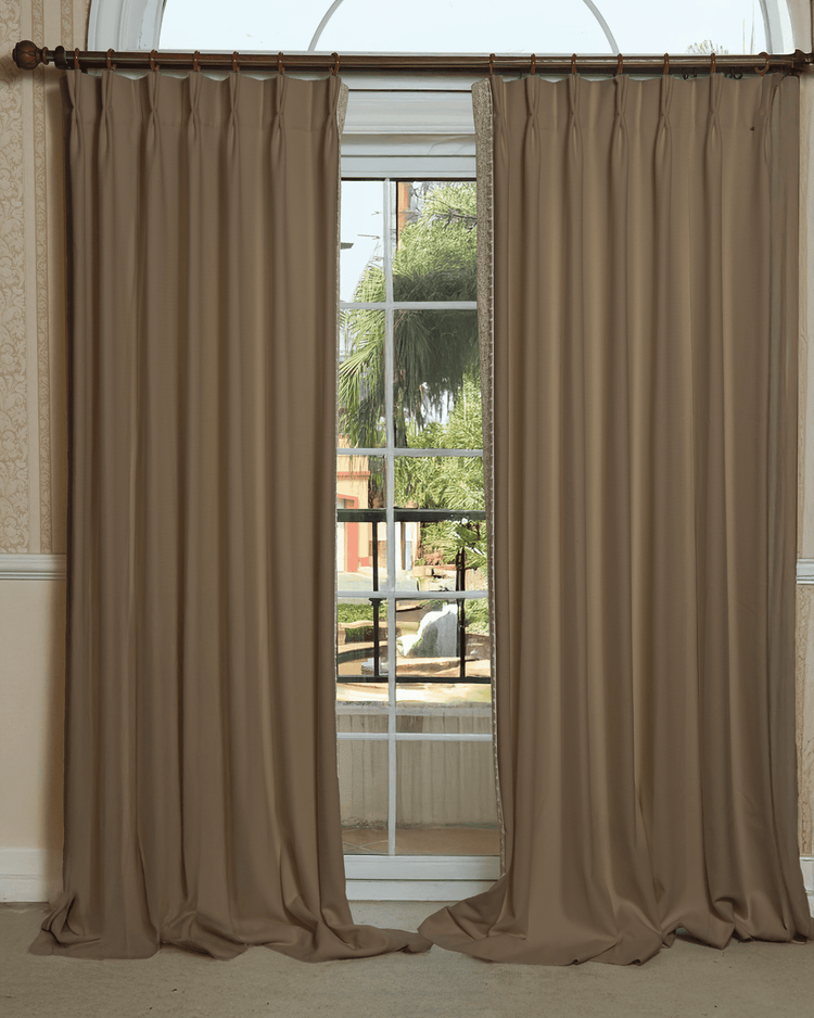 Zane Textured custom pinch pleat drapery in soft taupe with subtle trim, on a wooden rod over an arched window, enhancing home decor.