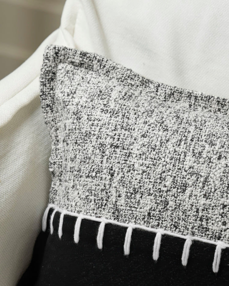 Close-up of Zane wool blend throw pillowcase, featuring textured grey & white marled fabric with decorative white yarn stitching above solid black.