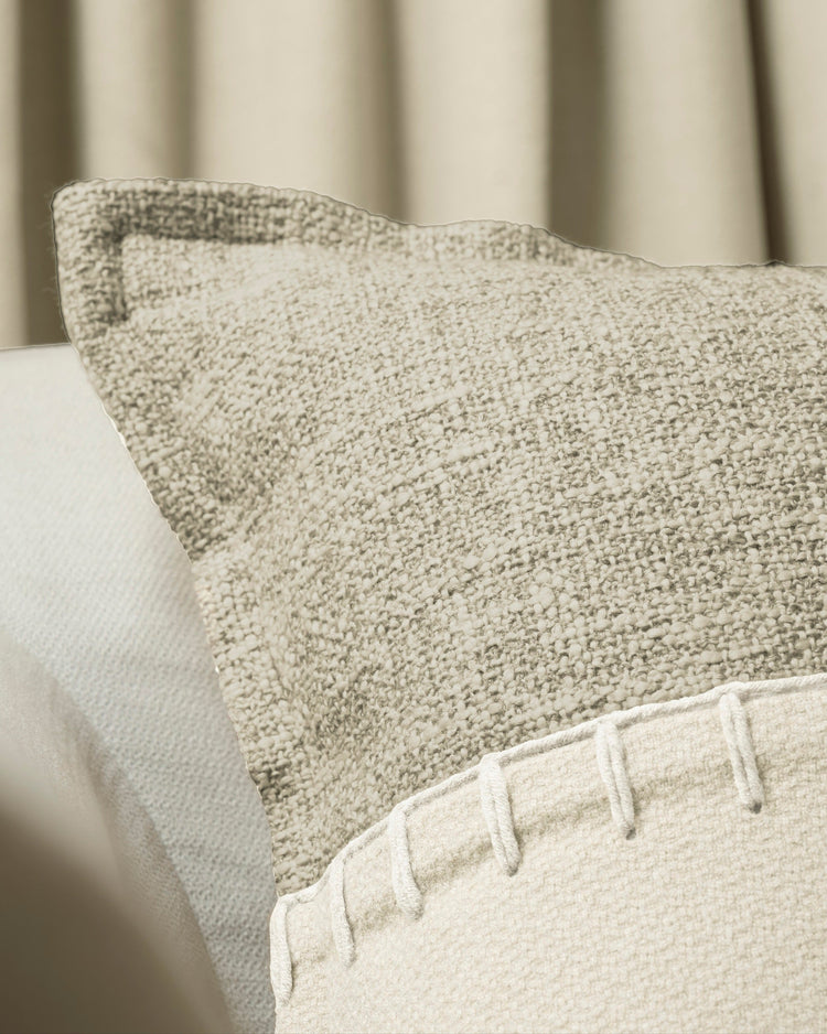 Detail of Zane Wool Blend lumbar pillowcase featuring textured fabric & chunky yarn stitching, with soft beige curtain backdrop.