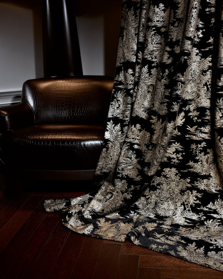 Zen foil printed black velvet custom curtain, designed in Italy, showcasing intricate gold patterns, draped beside a dark leather armchair.