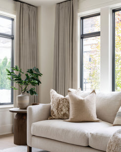Zoe linen look custom blackout curtains frame large windows, enhancing a neutral living room's sophisticated aesthetic.