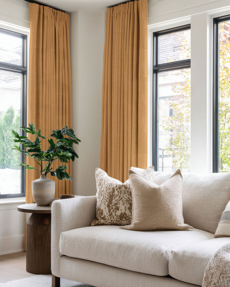 High-end golden-yellow blackout custom drapery with a linen look & pinch pleat header on tall windows, perfect for privacy.
