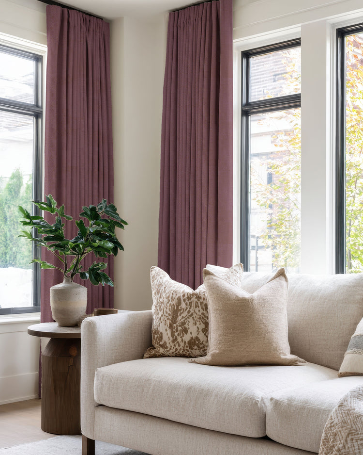 Zoe plum 100% blackout linen look custom pleated drapery for large windows in a bright living room with a cream sofa.