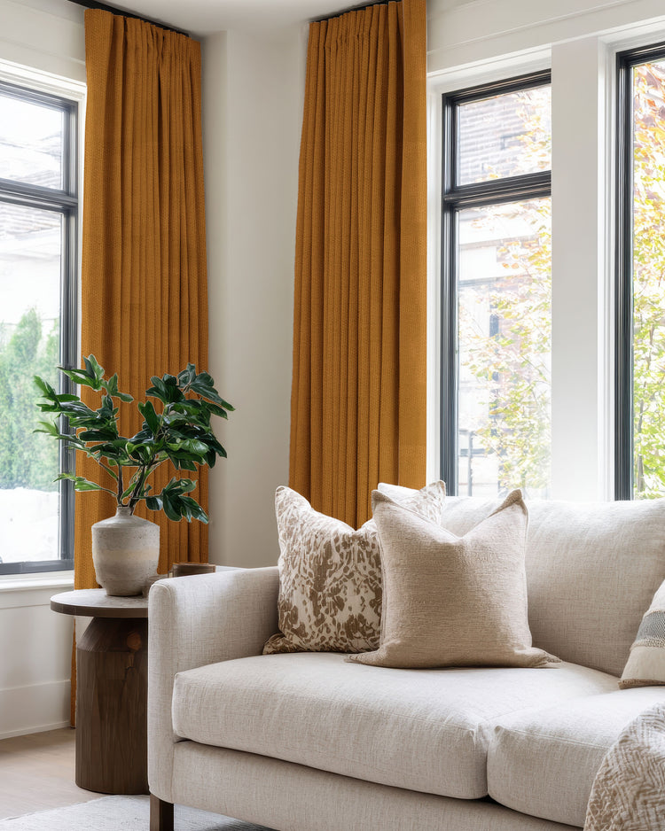 Zoe 100% blackout linen look custom curtains in vibrant orange, pinch-pleated, flank modern windows in a chic living room.