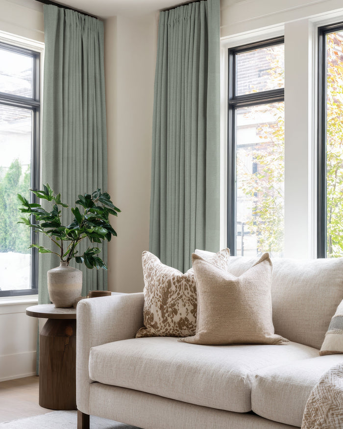 Elegant living room with custom Zoe 100% Blackout Linen Look drapery in serene green, offering optimal light control & privacy.