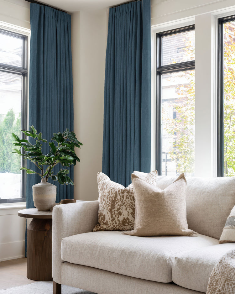 Zoe deep blue pleated blackout linen look custom drapery framing large windows, creating privacy in an elegant living room.